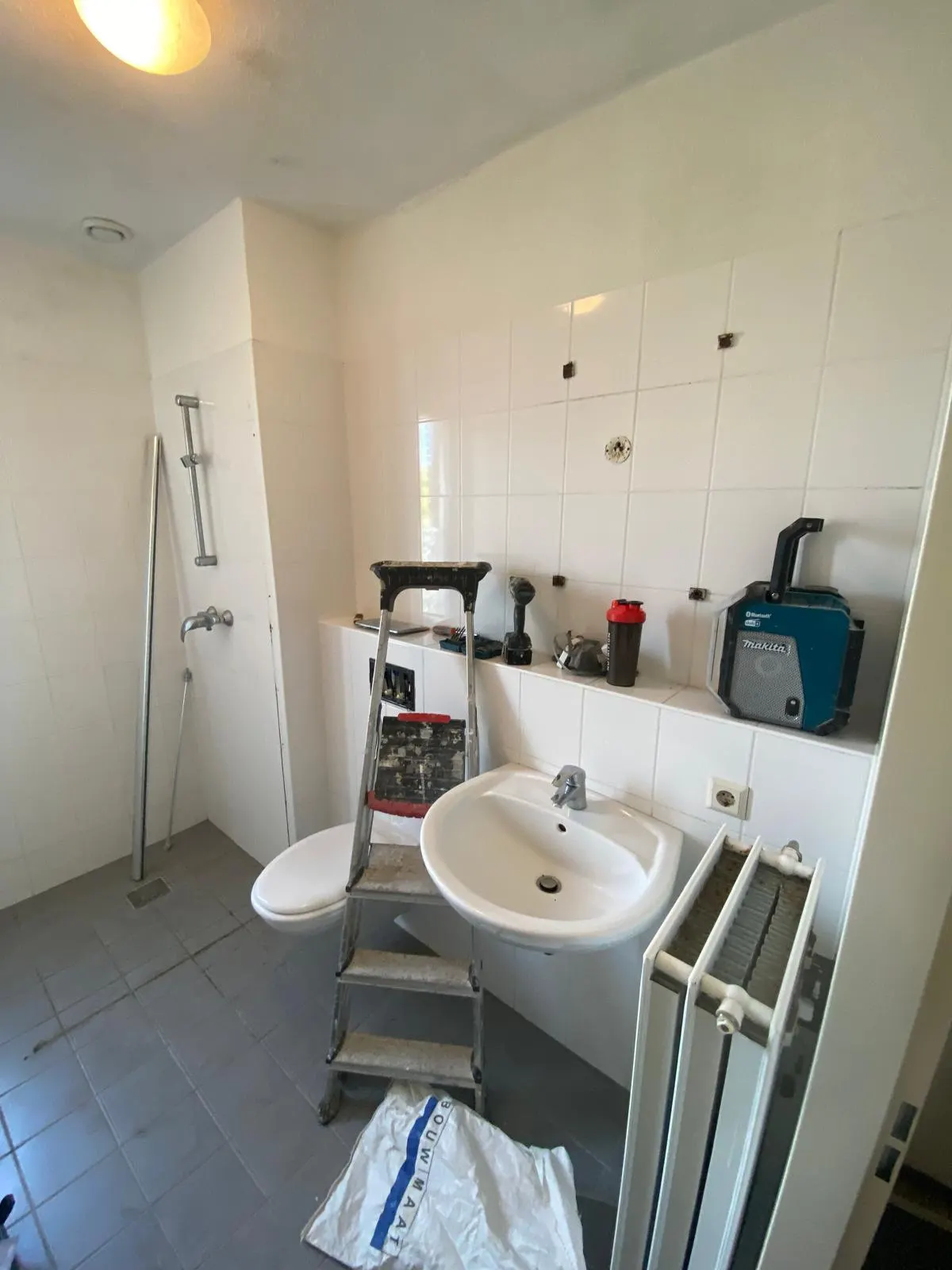 Kleine witte badkamer met open douchehoek, kranen en accessoires al verwijderd voor de renovatie