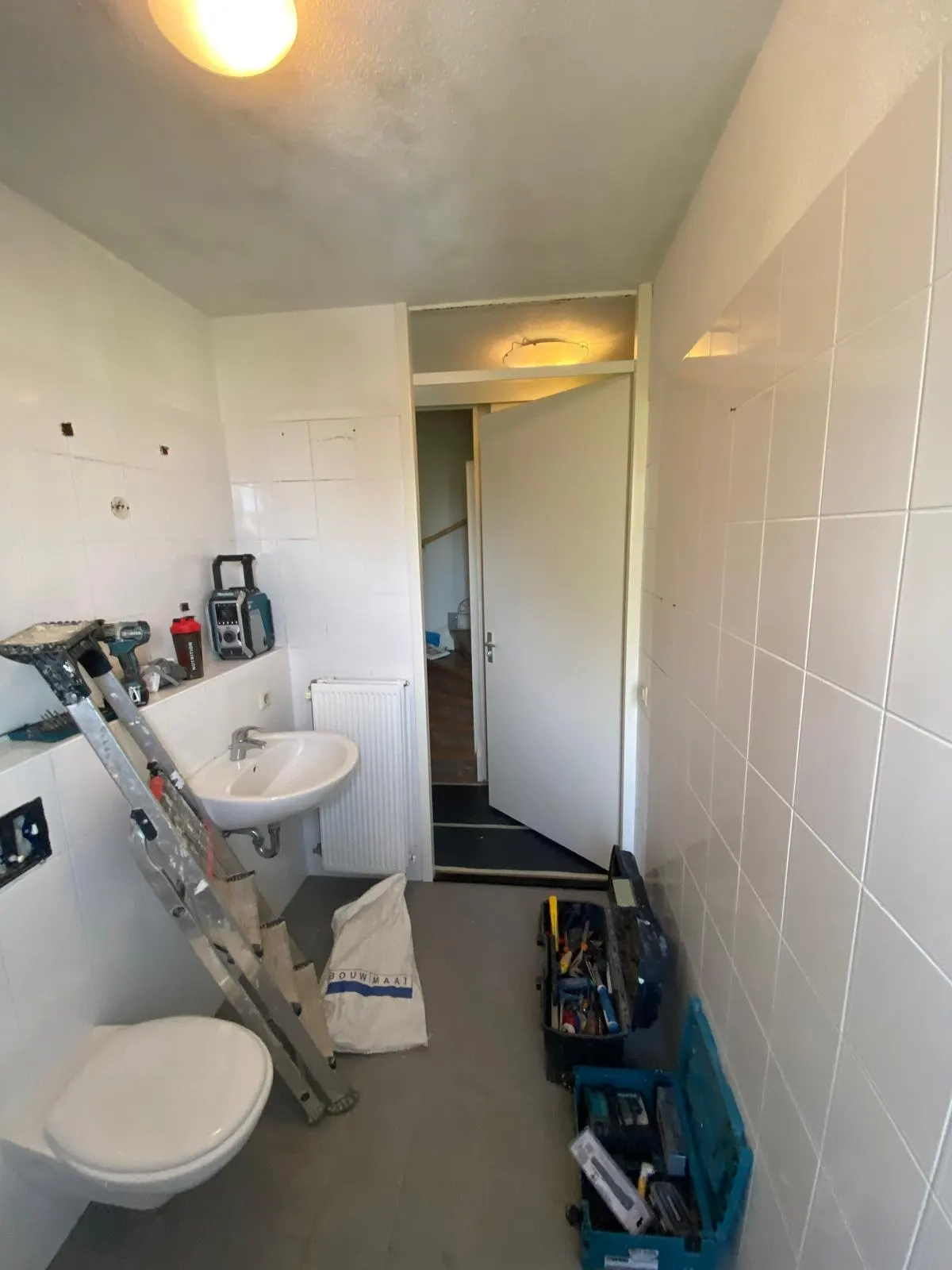 Kleine badkamer met hangend toilet, wastafel en radiator, gereedschap klaar voor de renovatie